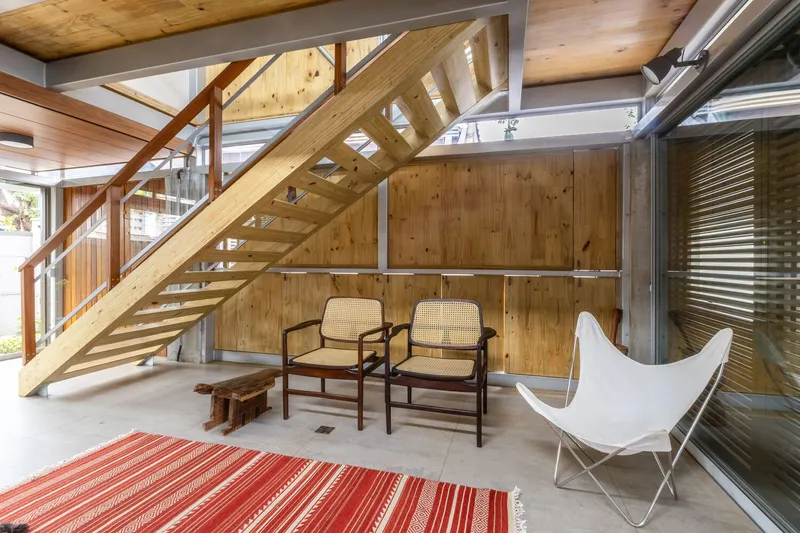 Open-tread timber staircase with glass guardrails rising through the double-height volume under clerestory windows