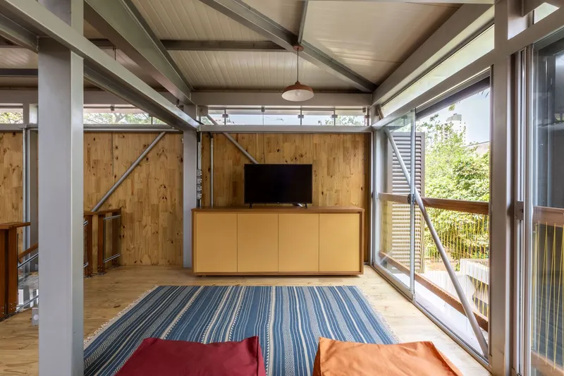 Mezzanine space with timber ceiling and diagonal steel bracing overlooking balcony through sliding glass doors