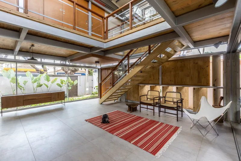 Double-height living area showing timber staircase mezzanine and planted courtyard visible through full-height glazing
