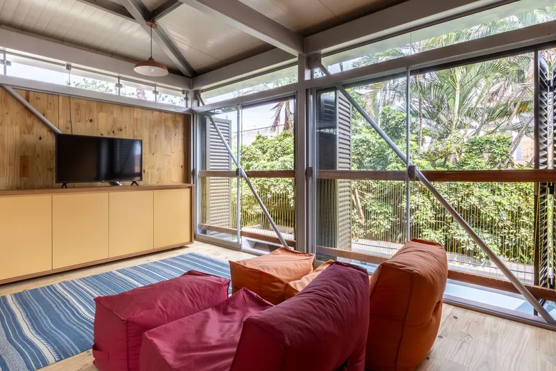 Living room with exposed steel beams and full-height glazing opening to a balcony with palm trees beyond