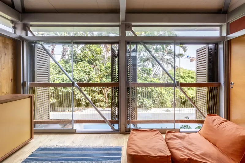 Interior view through sliding glass doors to an exterior terrace with louvered screens and tropical foliage