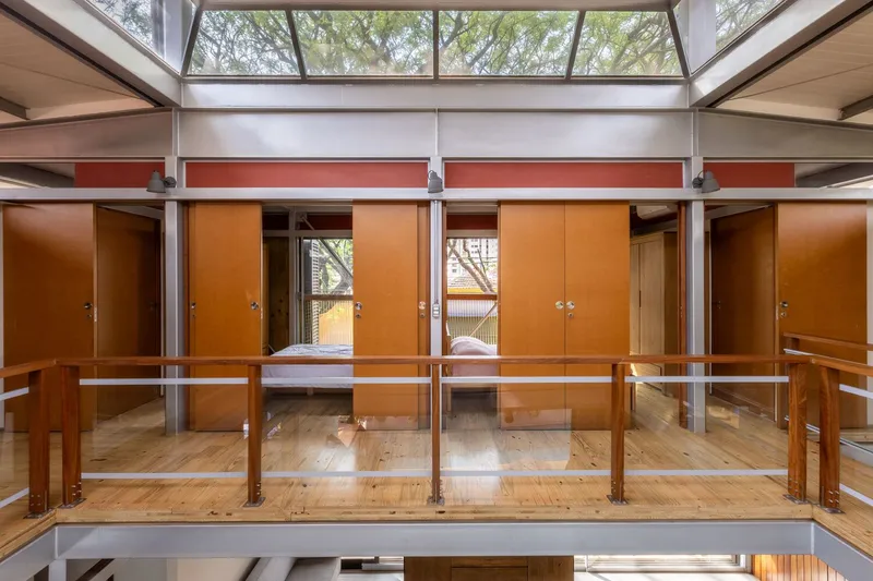 Mezzanine walkway with open timber cabinets and central doorway framing views to the screened balcony
