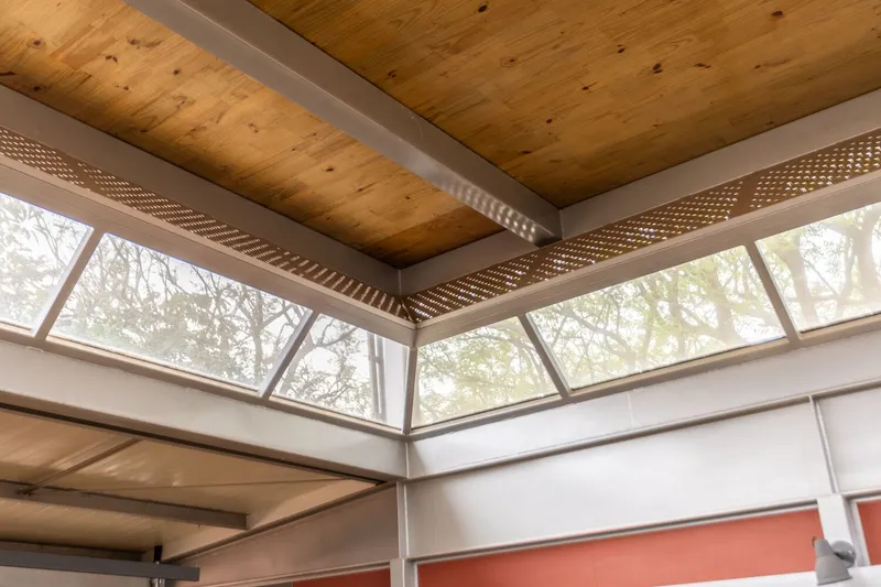 Clerestory window band with angled glazing and perforated ceiling panels beneath timber planks