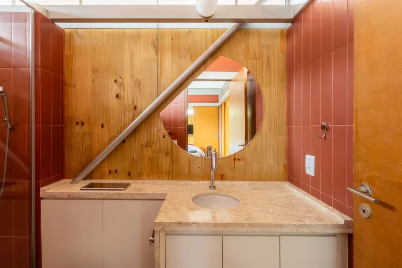 Bathroom vanity with circular mirror, timber paneling, and terracotta tiles beneath angled skylight