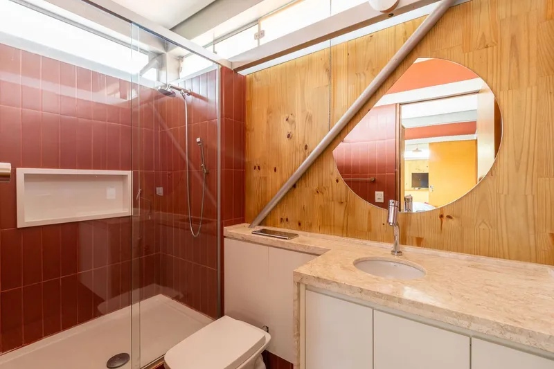Bathroom with glass shower enclosure, terracotta tiles, and timber-paneled wall with round mirror