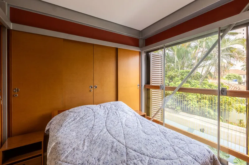 Bedroom corner showing sliding glass doors with louvered shutters and view to tropical vegetation