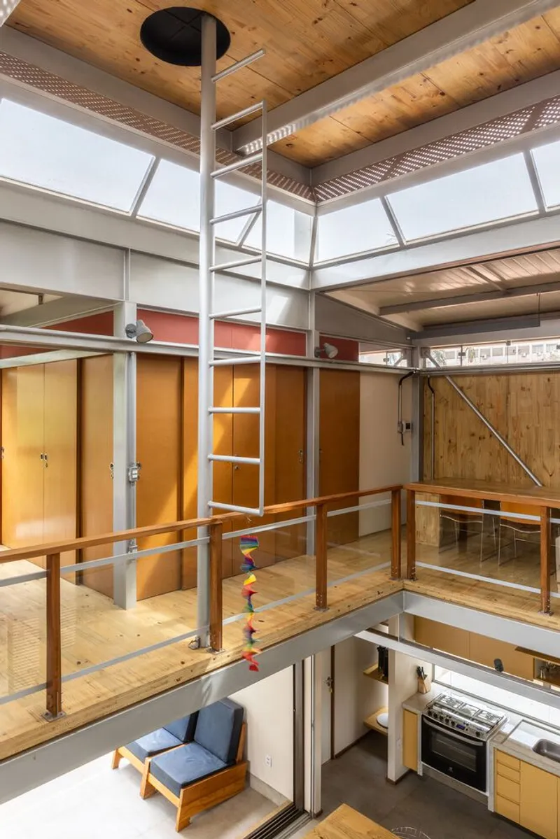 Double-height interior with exposed timber ceiling beams, central ladder, and mezzanine bridge with timber railing