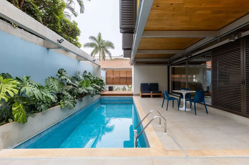 Narrow lap pool bordered by planted bed with tropical foliage and timber-slatted volume beyond