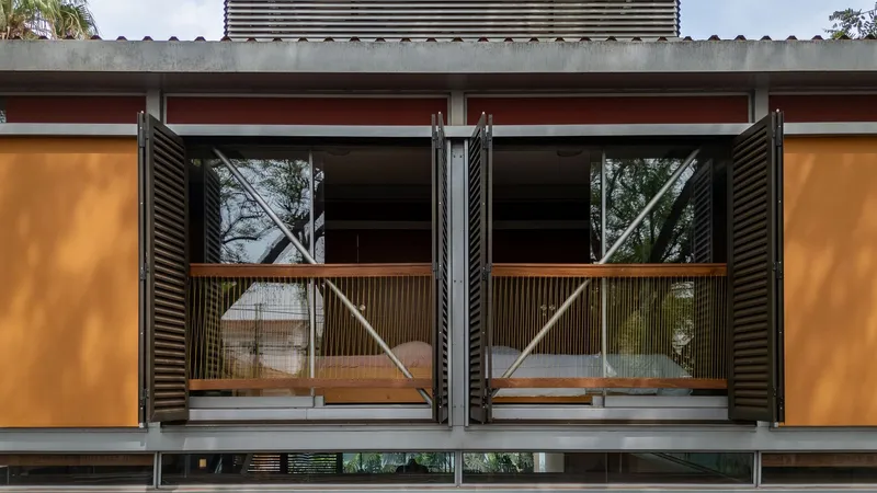 Upper floor balcony with black louvered shutters, timber railings, and orange panel facade in afternoon sun
