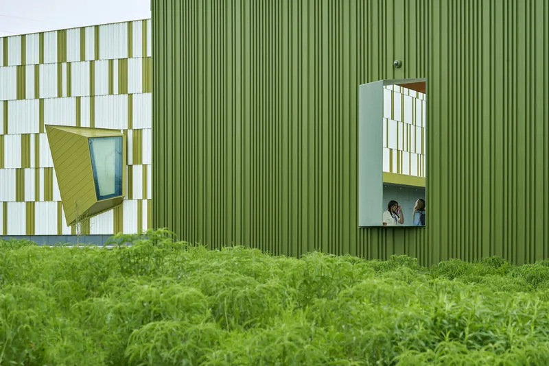 Facade detail showing vertical green louvers and pixelated white panels with an occupant visible through a trapezoidal window