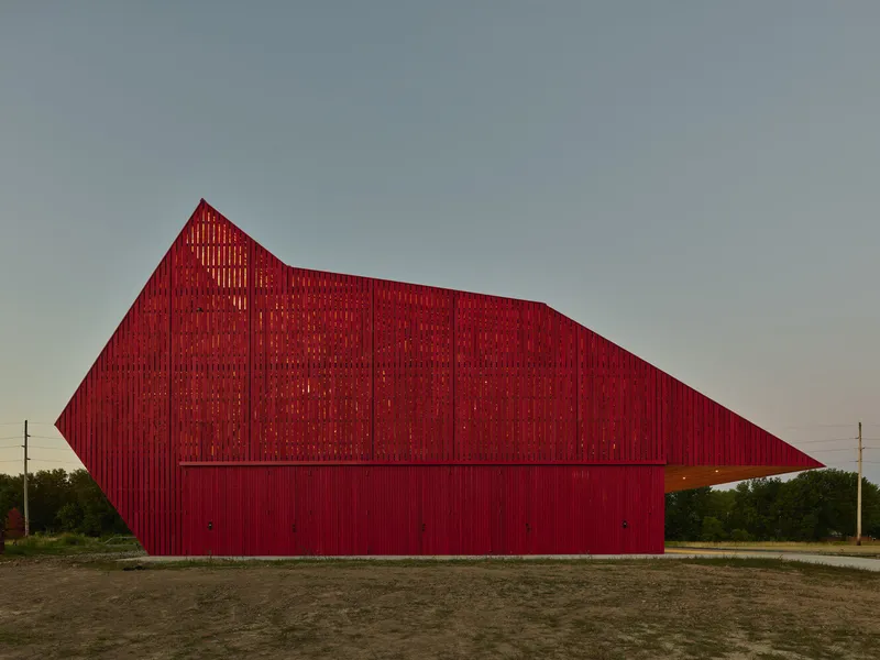 Perforated red metal facade with cantilevered roofline at twilight