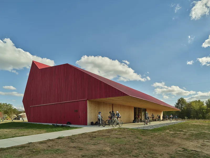 Covered porch with timber cladding and red metal roof as cyclists gather beneath