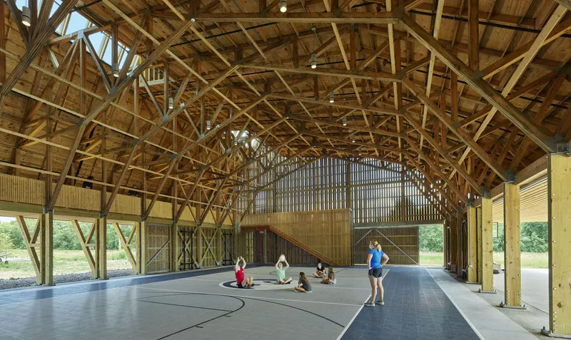 Exposed timber truss roof structure spanning a basketball court where several people sit in a circle