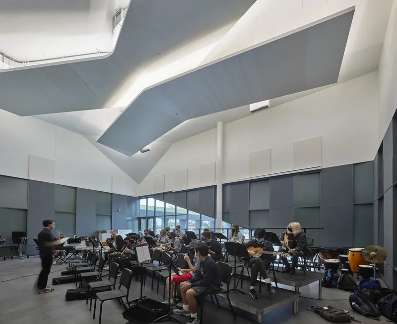 Rehearsal room with folded ceiling plane admitting daylight over musicians seated with a person walking past