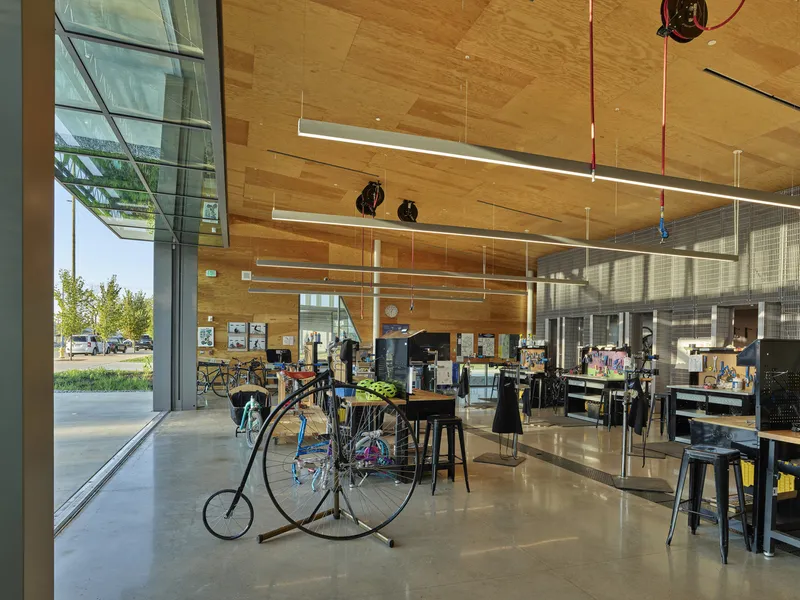 Lobby with timber ceiling and concrete floor displaying a vintage high-wheel bicycle near glass-walled display cases