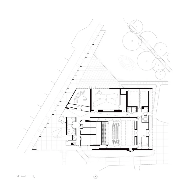 Site plan drawing showing two angled building volumes with a central auditorium and surrounding landscape