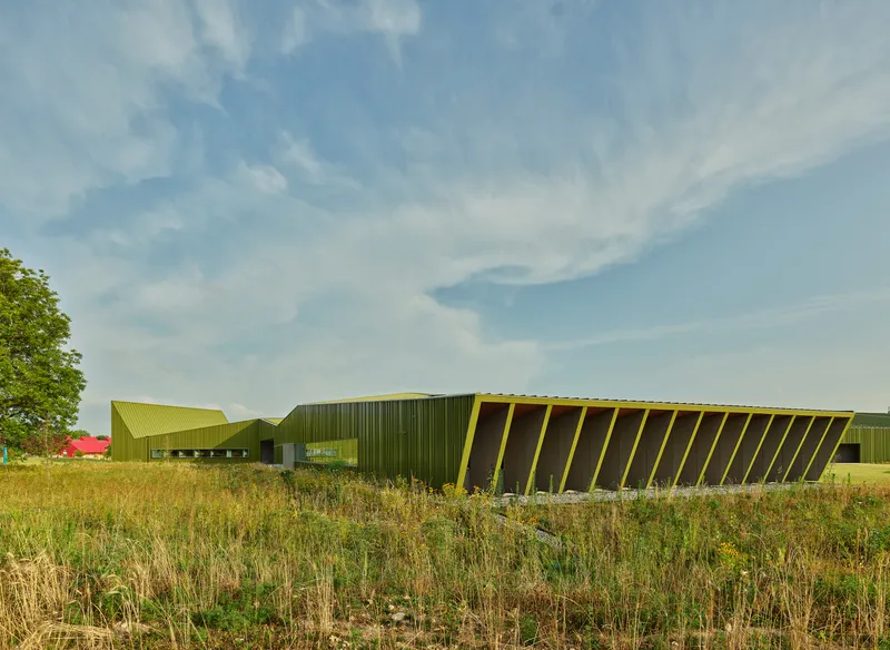 Angled facade with vertical yellow metal fins and glazing in a dry prairie landscape