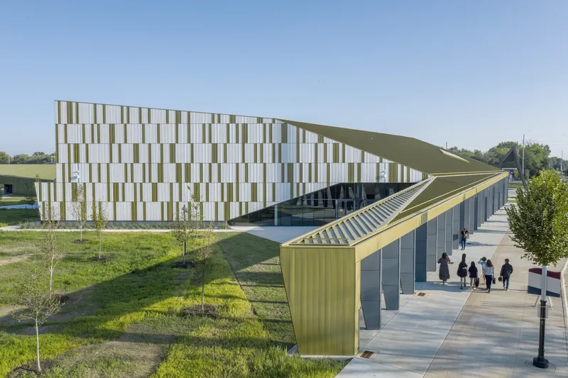 Angled view of the white and olive panel facade with a planted green roof and pedestrians on the sidewalk
