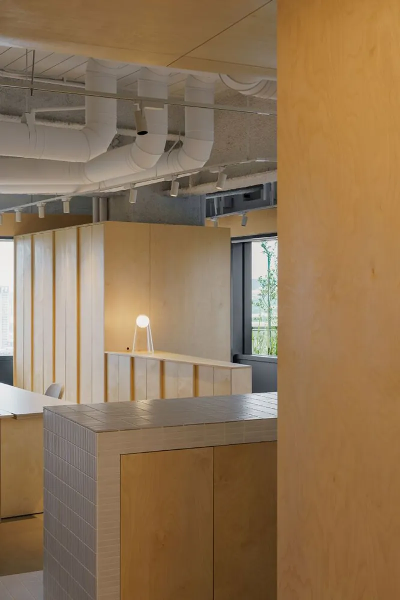 Office interior with plywood millwork and exposed white ductwork running beneath the concrete ceiling