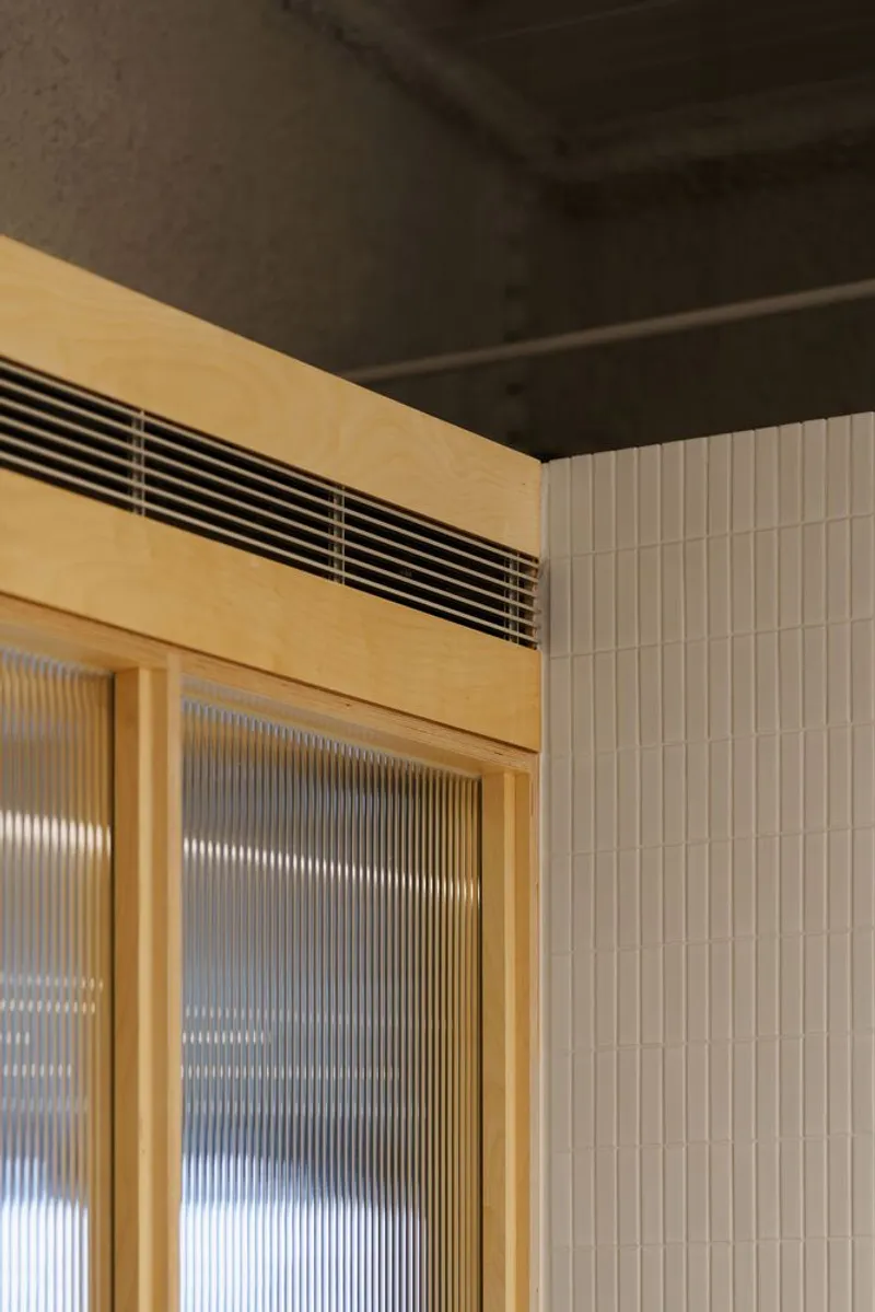 Timber-framed partition with reeded glass panels and horizontal ventilation grille mounted above the frame