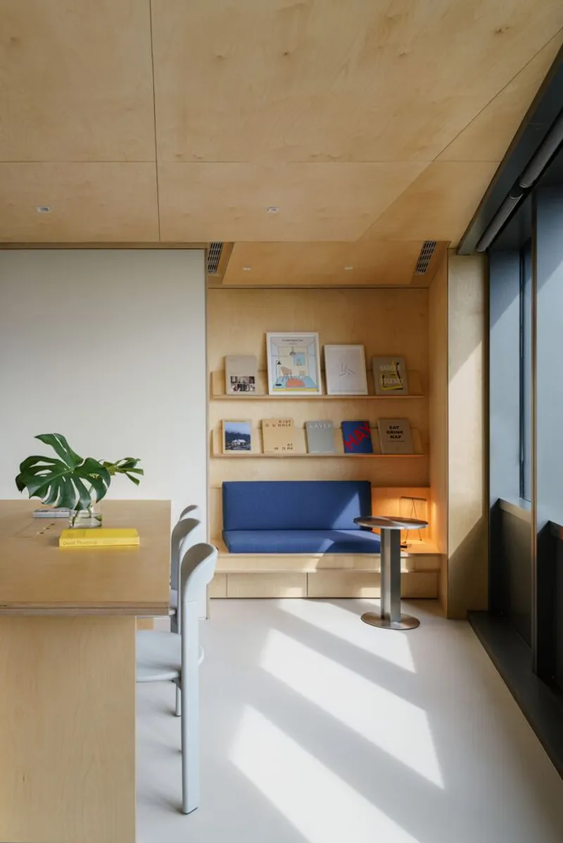 Plywood-lined reading nook with blue bench cushion and display shelves in afternoon sunlight