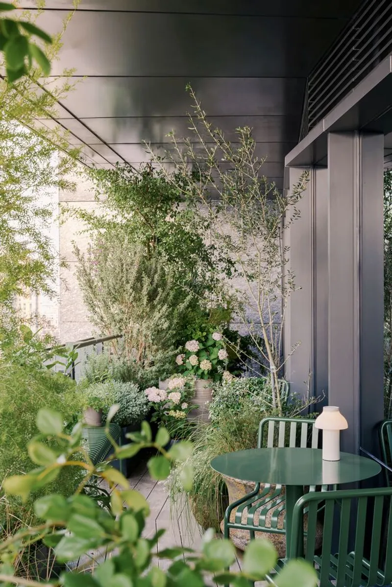 Outdoor terrace with green metal table and chairs surrounded by potted plants and climbing vines