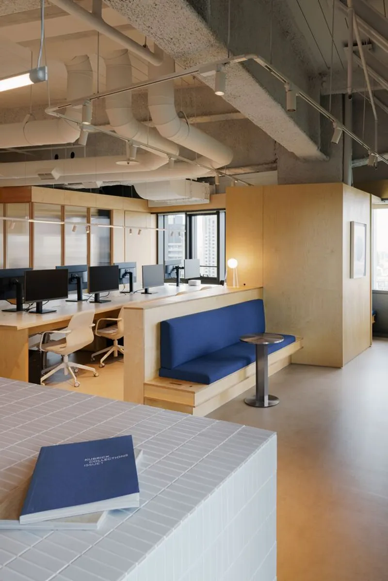 Open office area with integrated blue upholstered bench seating and exposed mechanical systems overhead
