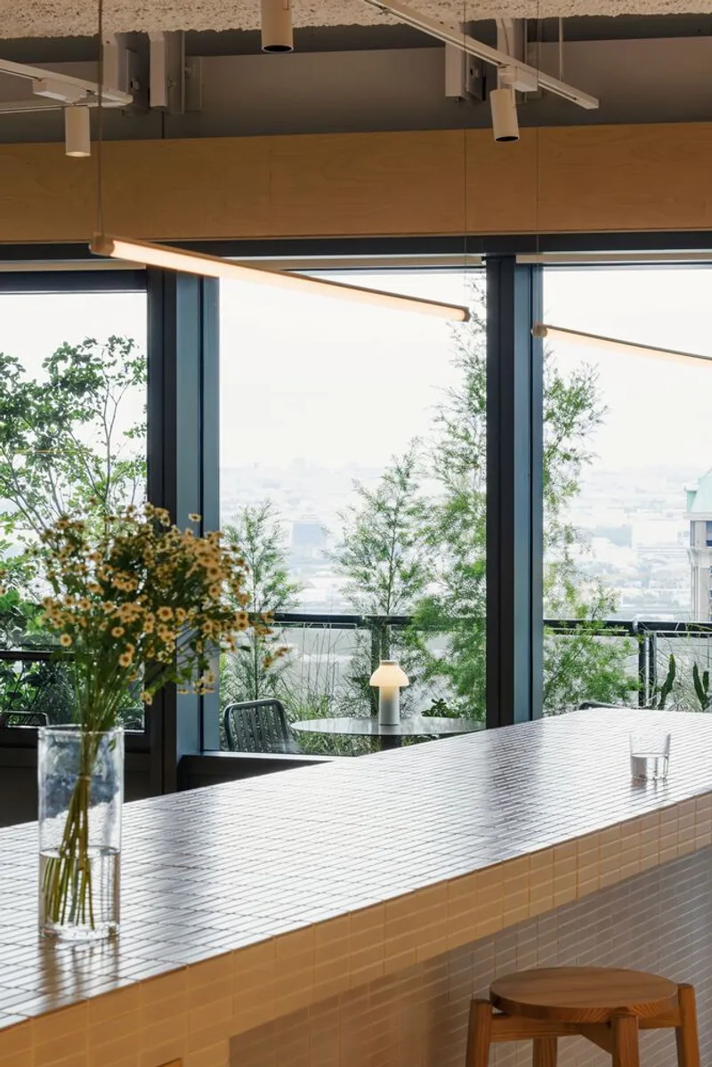 Timber kitchen island with ribbed metal counter surface looking toward floor-to-ceiling windows and planted terrace beyond