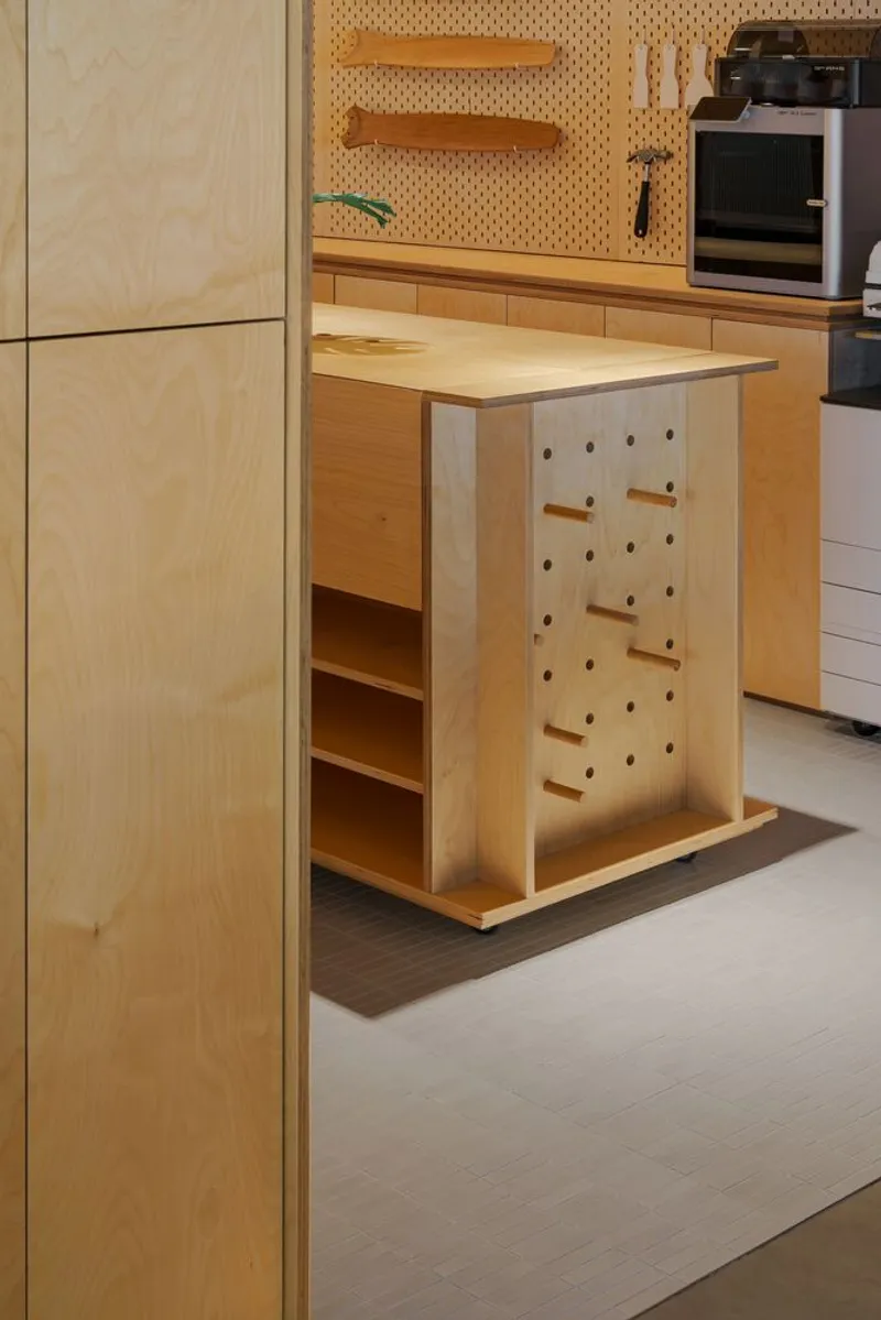 Mobile plywood cart with pegboard panel and wooden dowel hooks facing built-in shelving and appliances
