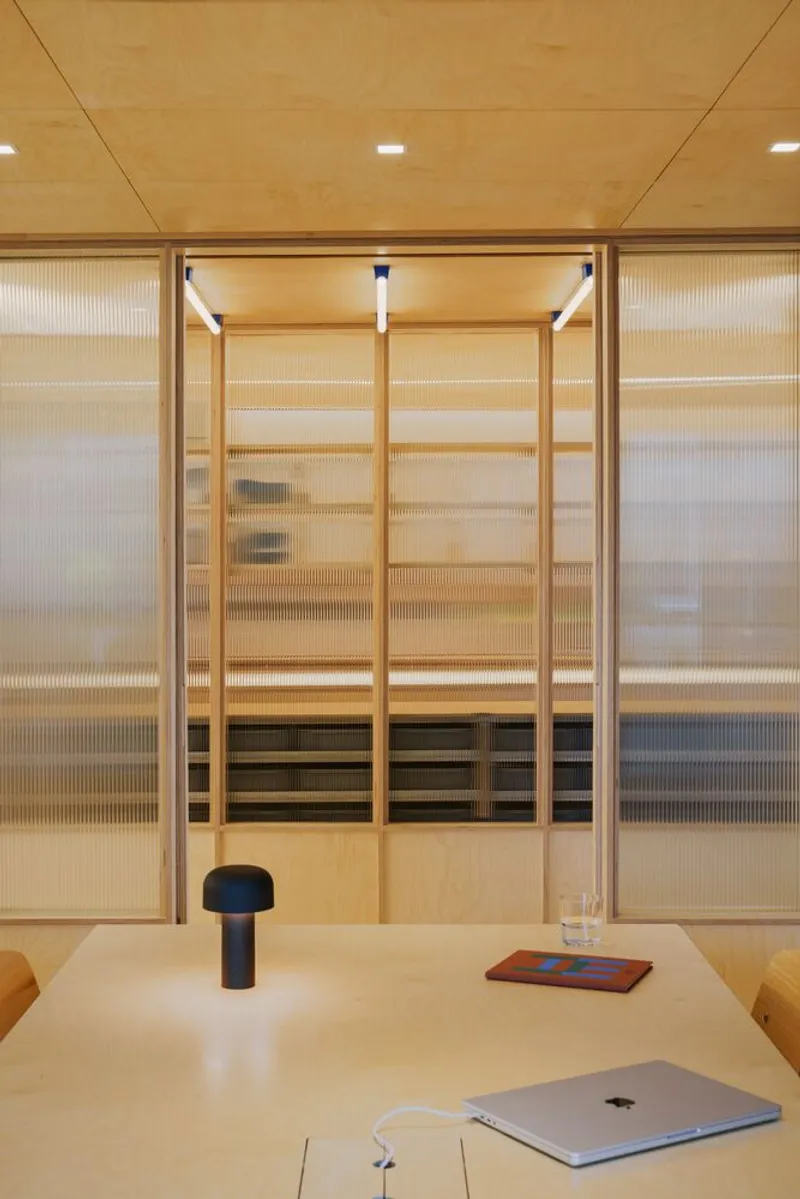 Close-up of translucent fluted glass partition with timber framing and horizontal wood shelving visible through the glazing