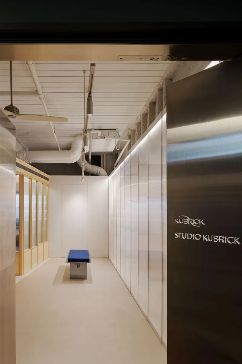 Reception hallway with single bench against white wall beneath exposed ductwork and horizontal plank ceiling
