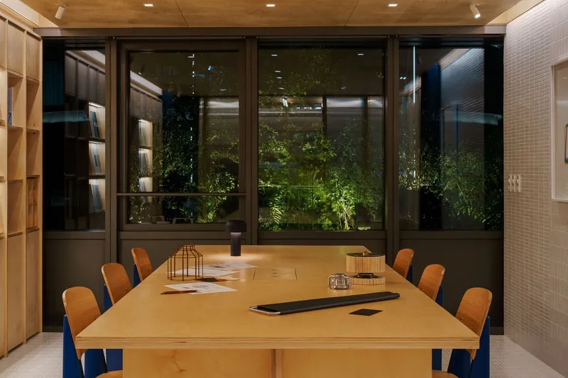 Conference table facing exterior glazing with illuminated planted courtyard visible beyond at night