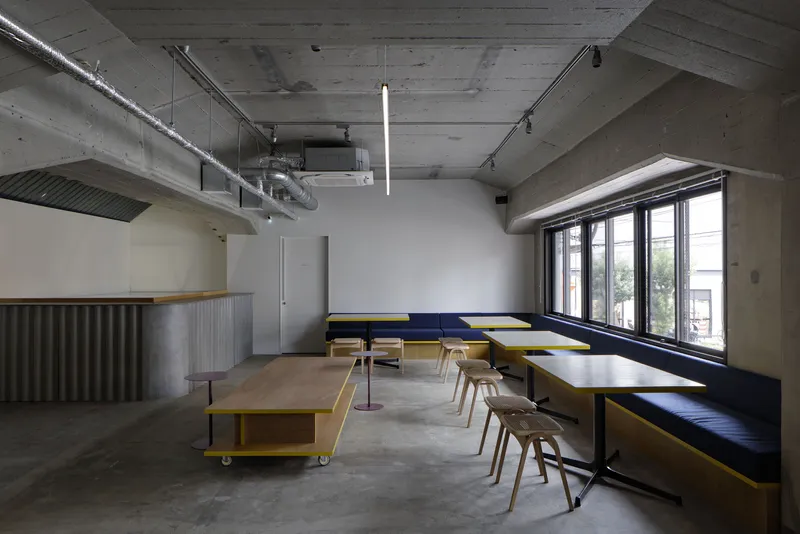 Seating area with concrete ceiling, blue banquette along windows, and mobile yellow tables on casters