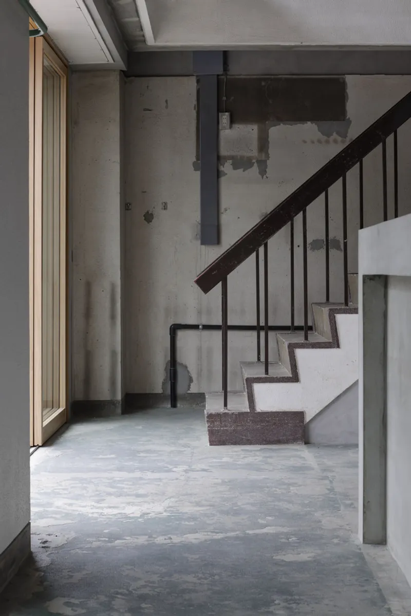 Corner view of steel staircase with vertical balusters ascending beside bare concrete columns