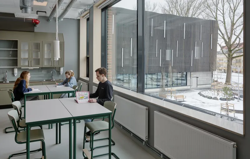 Dining area with green steel tables and chairs overlooking a snowy courtyard through floor-to-ceiling windows