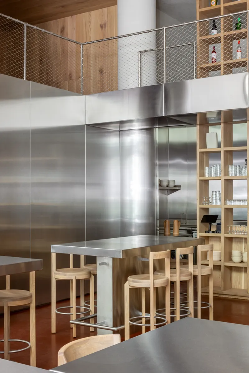 Corner view of the stainless steel panels with mesh-guarded mezzanine and timber shelving above