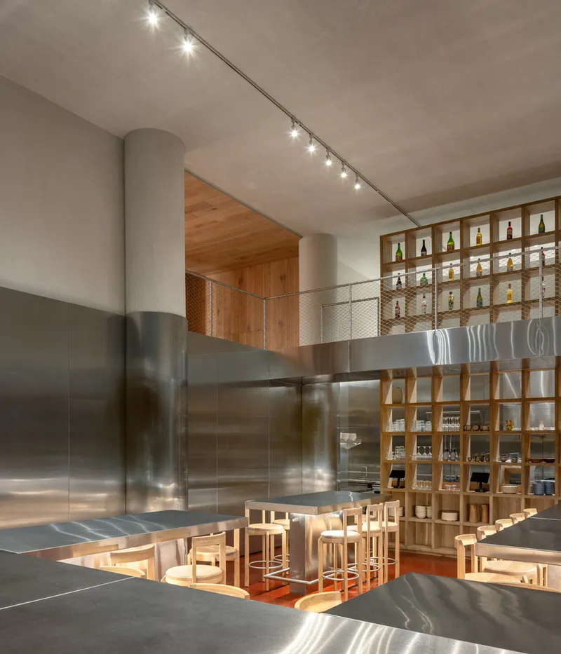 Double-height interior with curved metal column and light wood display shelving above seating area