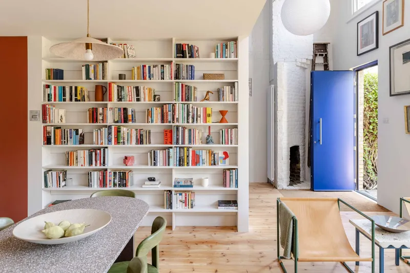 Floor-to-ceiling white bookshelf wall separating dining area from the blue entry door beyond