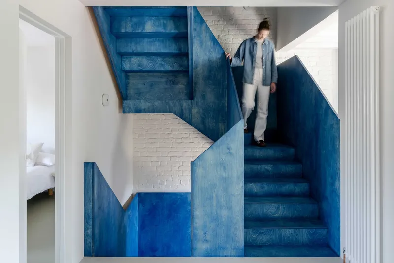 Blue-painted plywood staircase with person ascending against white brick wall