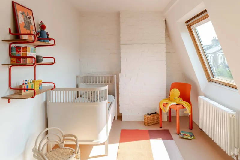 Nursery room with sloped ceiling and roof window illuminating pale plywood paneling