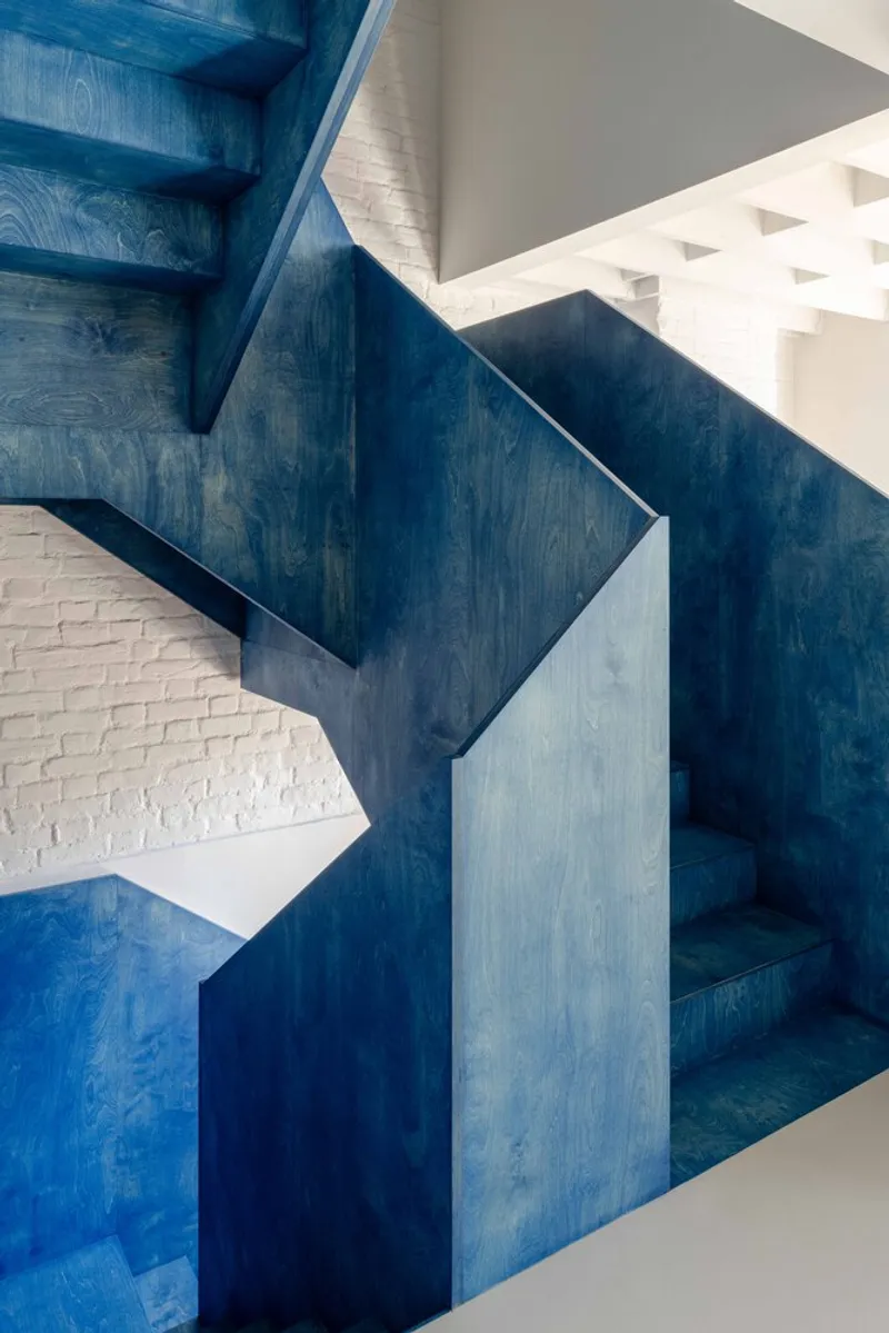 Blue-stained timber staircase wrapping around white painted brick walls in bright daylight
