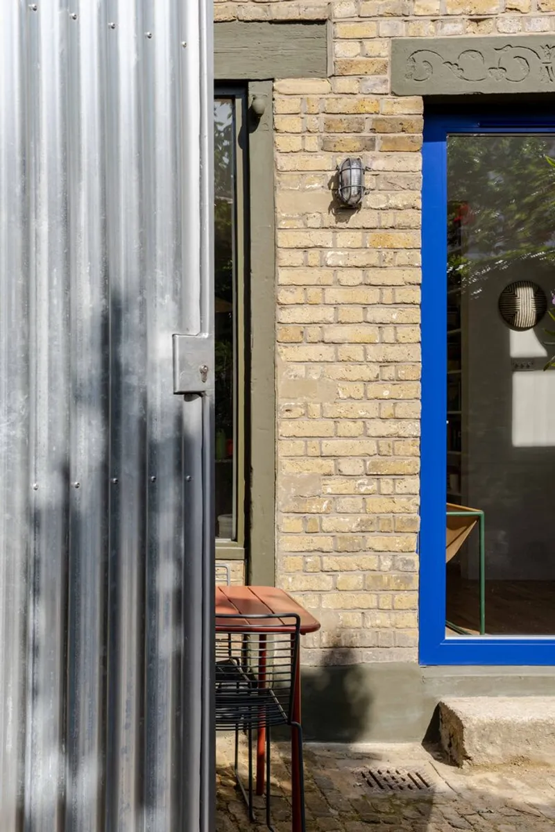 Corrugated metal siding meeting yellow brick wall with blue window frame in afternoon sun