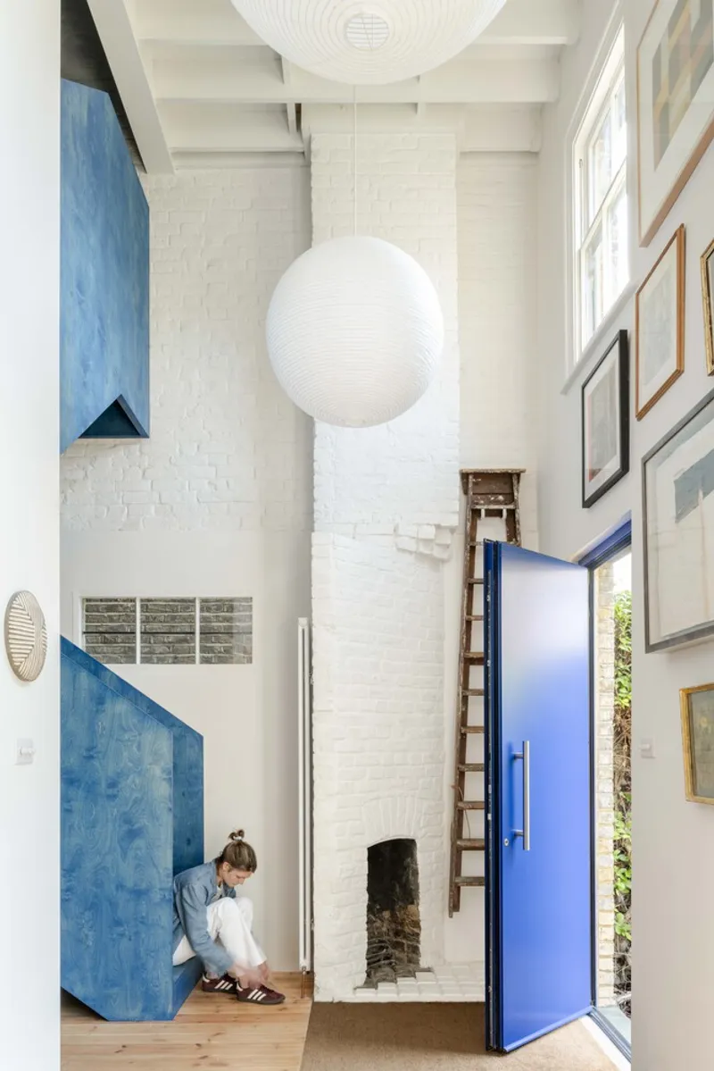 Double-height living space with painted white brick chimney and a child descending timber stairs