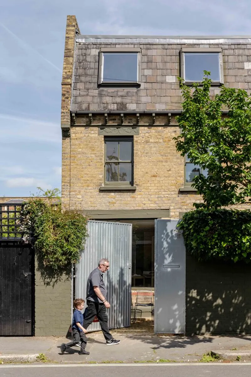 Street facade showing yellow brick above a corrugated metal ground floor with two residents passing