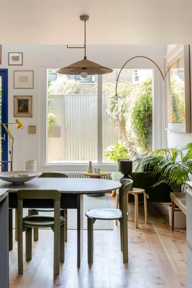 Dining area with pendant fixtures overlooking a courtyard with corrugated metal fencing and climbing plants