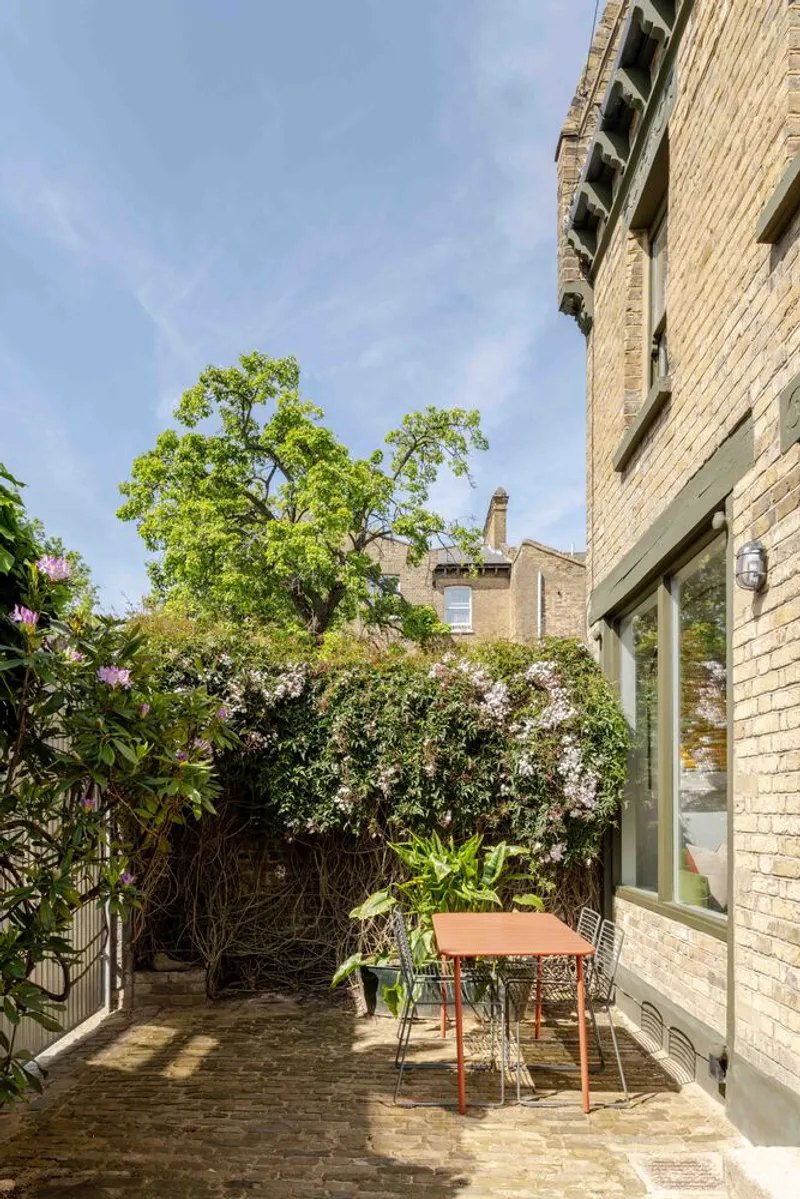 Rear courtyard patio with orange metal furniture beneath a mature tree and yellow brick walls