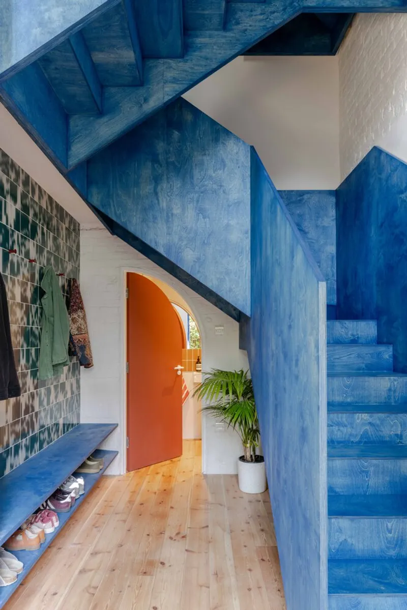 Entry hall with blue-stained timber staircase and plywood beneath an exposed structural soffit