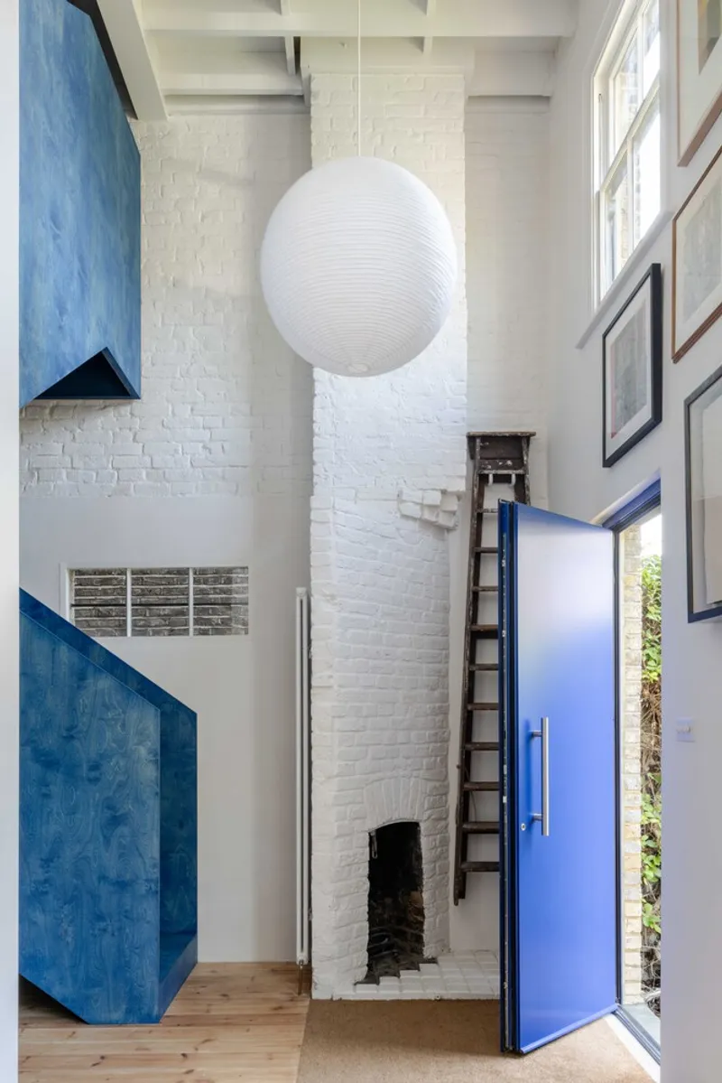 Double-height entryway with painted white brick fireplace and blue door opening to planted exterior
