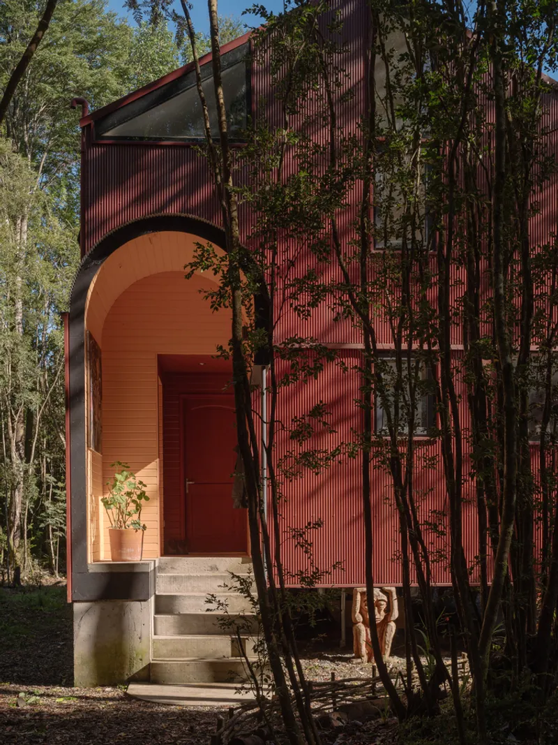 Red corrugated metal facade with arched entryway and concrete steps nestled among eucalyptus trees