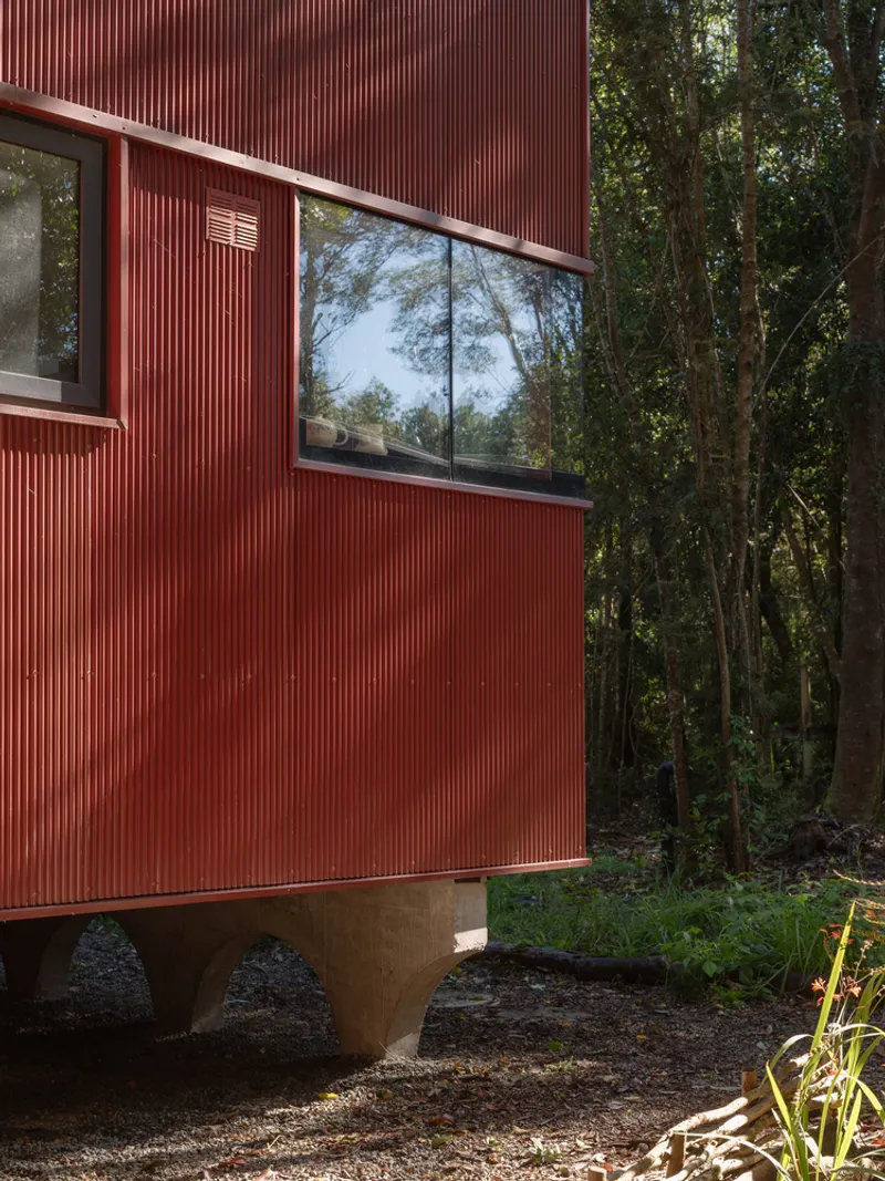 Red corrugated metal facade with horizontal window band reflecting surrounding trees